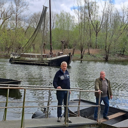Die zwei Männer stehen am Wasser. Im Hintergrund ist das Schiff zu sehen.