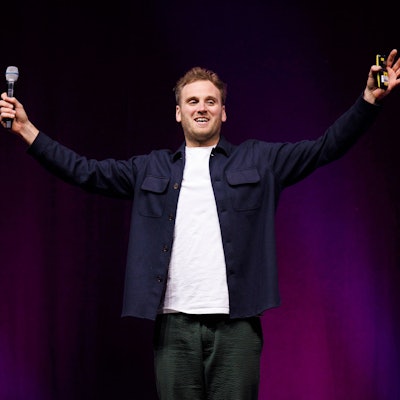 Psychologe und Autor Leon Windscheid steht mit ausgebreiteten Armen in der Lanxess-Arena. Er trägt ein weißes T-Shirt und ein blaues Hemd.