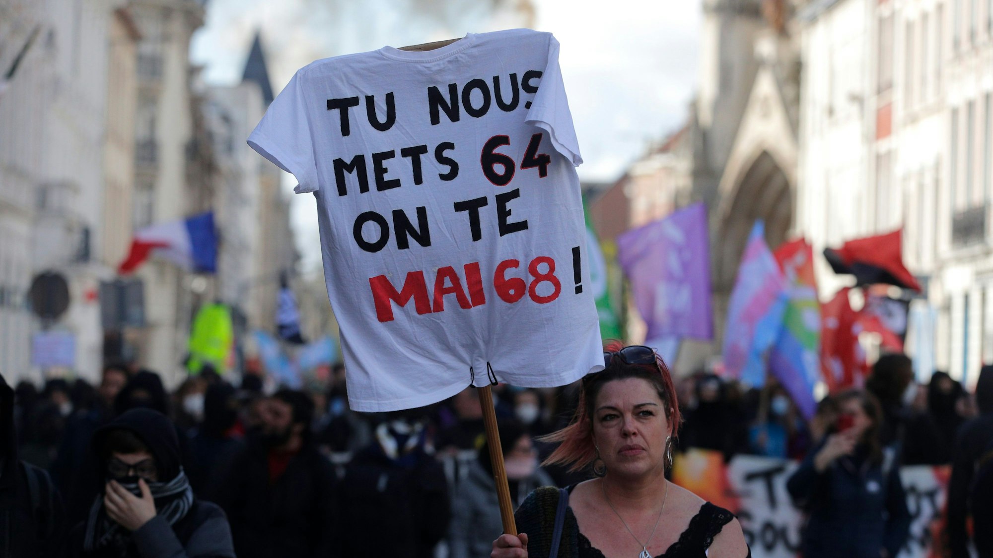 Eine Frau hält ein T-Shirt mit der Aufschrift „Ihr verhängt 64 Jahre, wir wiederholen Mai 68“ während einer Demonstration.