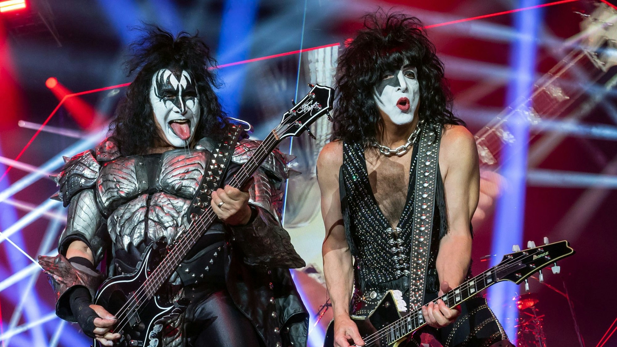 Gene Simmons und Paul Stanley von der US-amerikanischen Hard-Rock-Band Kiss bei einem Auftritt auf der Bühne. Sie halten E-Gitarren in der Hand.