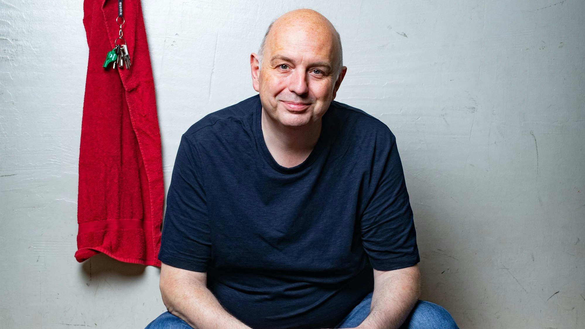 Der Autor Frank Goosen sitzt auf einer Bank und lächelt in die Kamera.