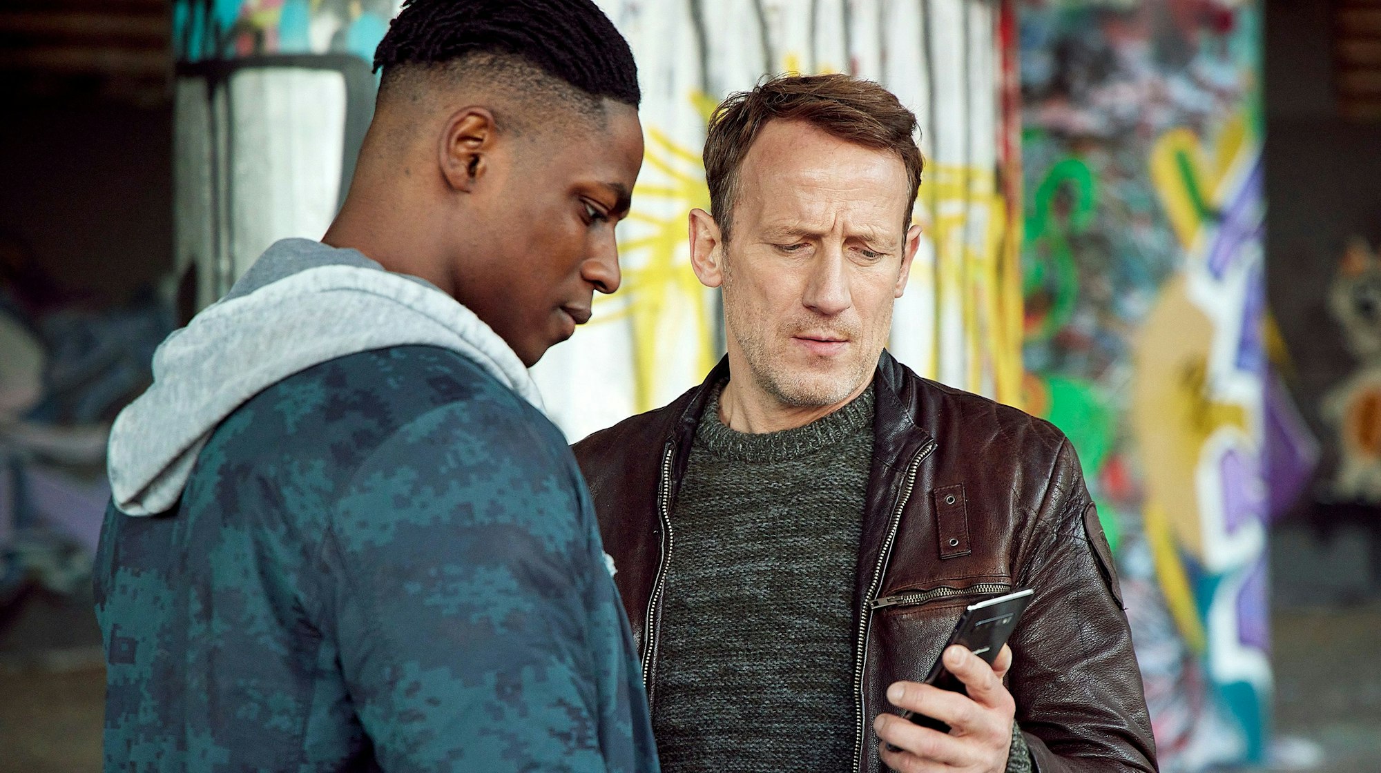 „Tatort“-Kommissar Thorsten Falke (Wotan Wilke Möhring) zeigt Sam ein Bild des Toten auf seinem Handy.