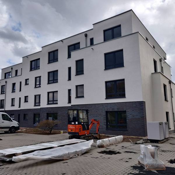 Ein Neubau. Im Vordergrund ist ein kleiner Bagger und der Lieferwagen einer Baufirma zu sehen.