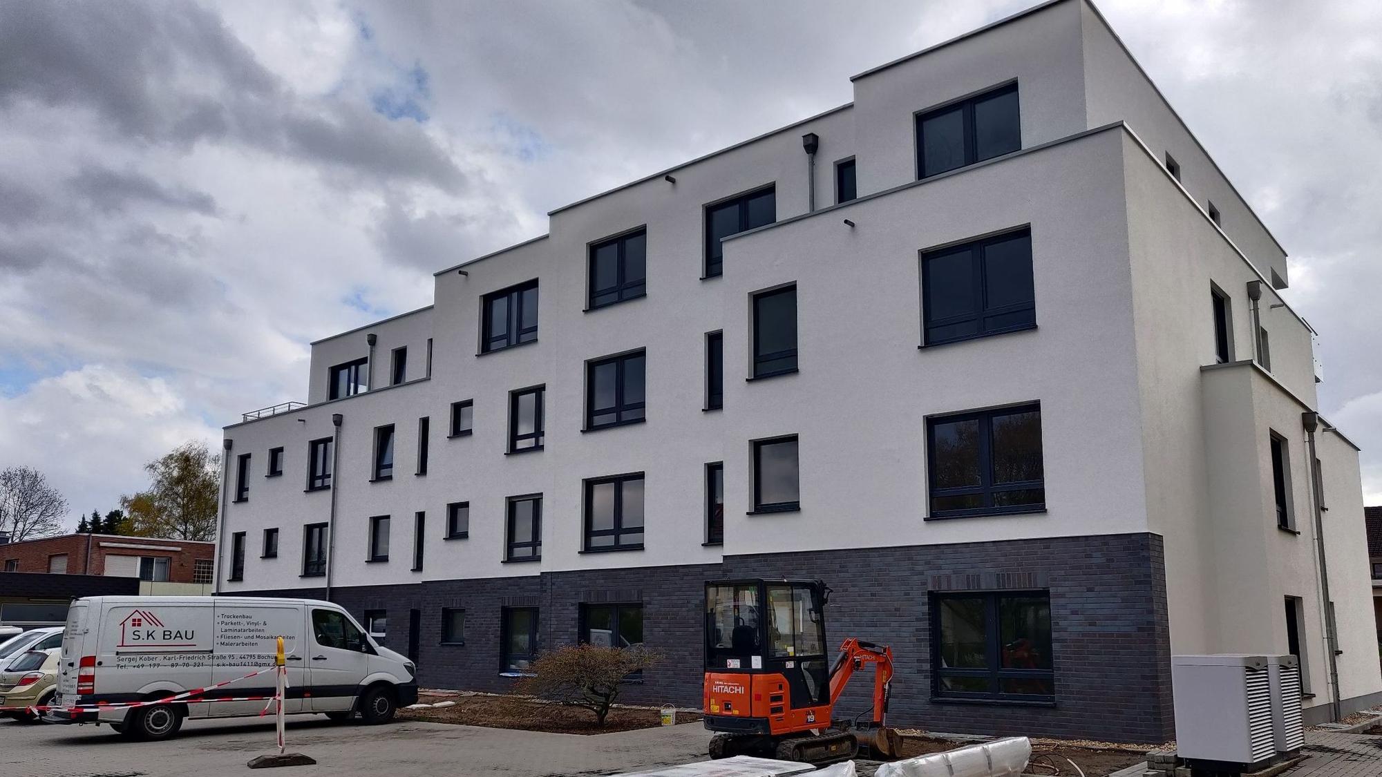 Handwerkerfahrzeuge parken vor der Baustelle für ein dreistöckiges Mehrfamilienhaus.
