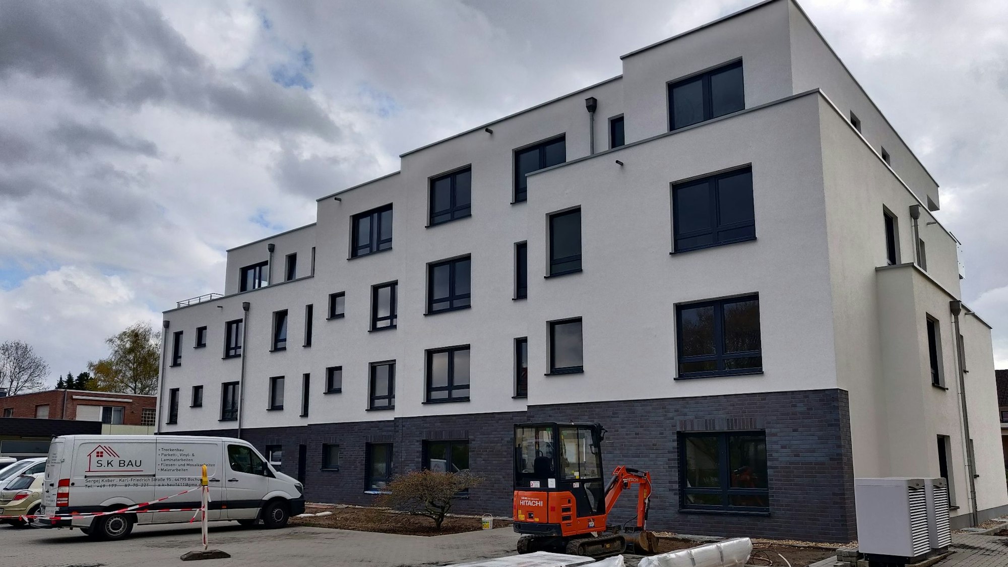Handwerkerfahrzeuge parken vor der Baustelle für ein dreistöckiges Mehrfamilienhaus.