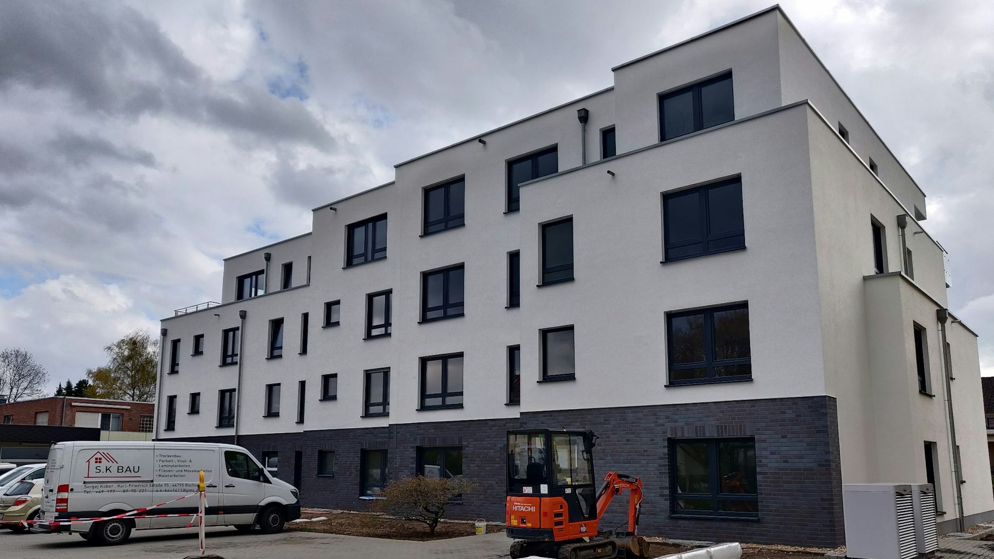 Ein Neubau. Im Vordergrund ist ein kleiner Bagger und der Lieferwagen einer Baufirma zu sehen.