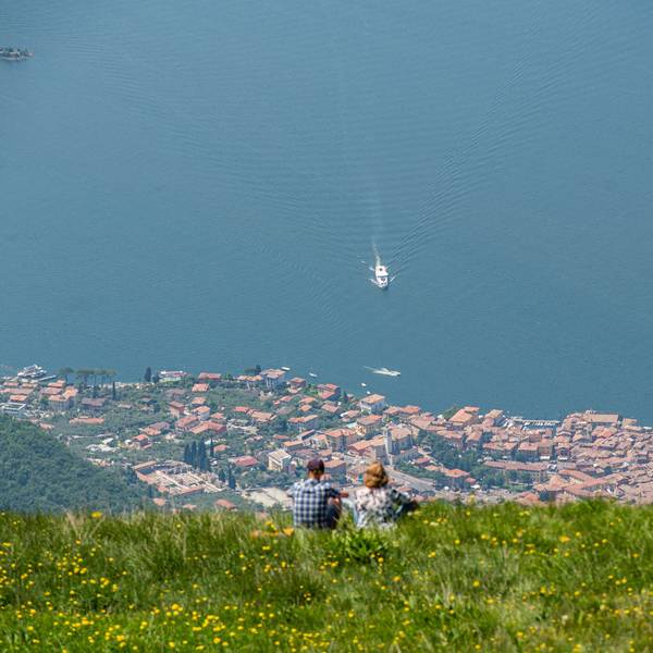 Blick vom Berg Monte Baldo auf den Gardasee und den Ort Malcesine. Auf dem See ist ein weißes Boot unterwegs.