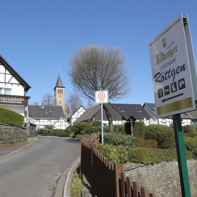 Ein Fachwerkhaus liegt an einer Straße, im Hintergrund ist eine Kirche zu sehen.