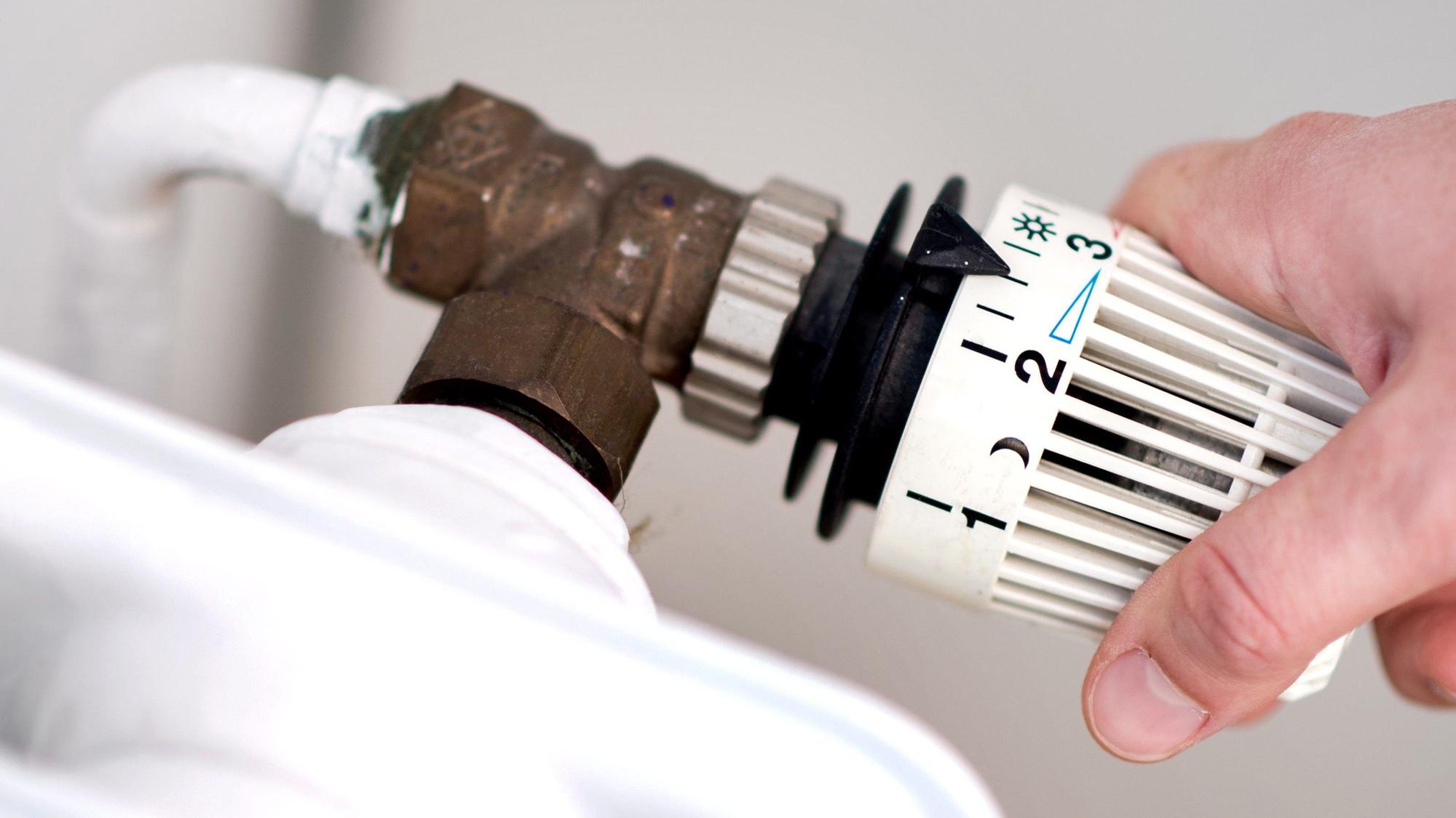Eine Frau dreht am Thermostat einer Heizung. (Symbolbild)