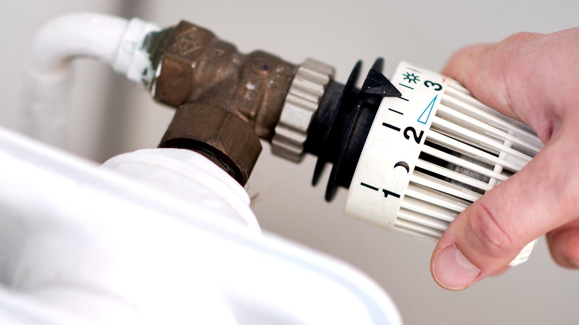 Eine Frau dreht am Thermostat einer Heizung.