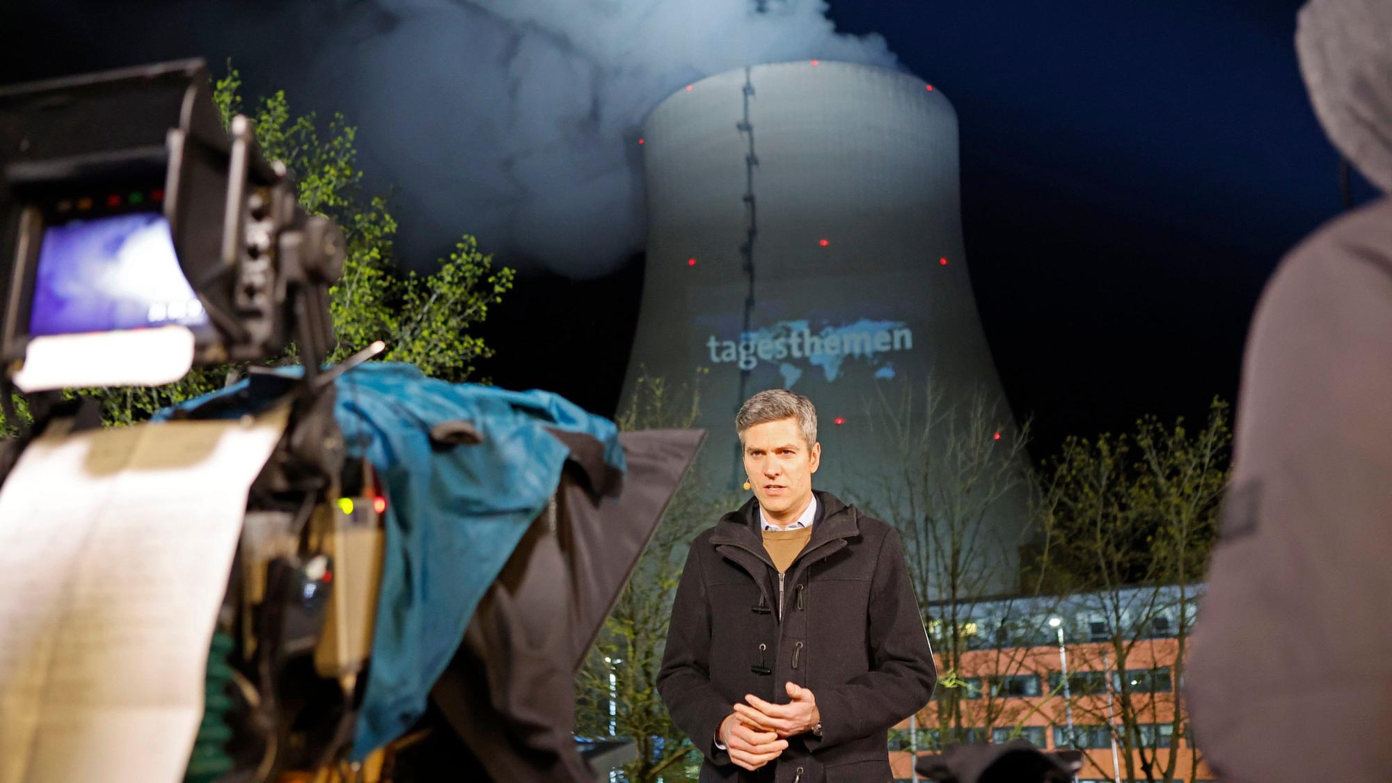 „Tagesthemen“-Moderator Ingo Zamperoni steht auf einem Balkon vor dem Kühlturm des AKW Isar 2.