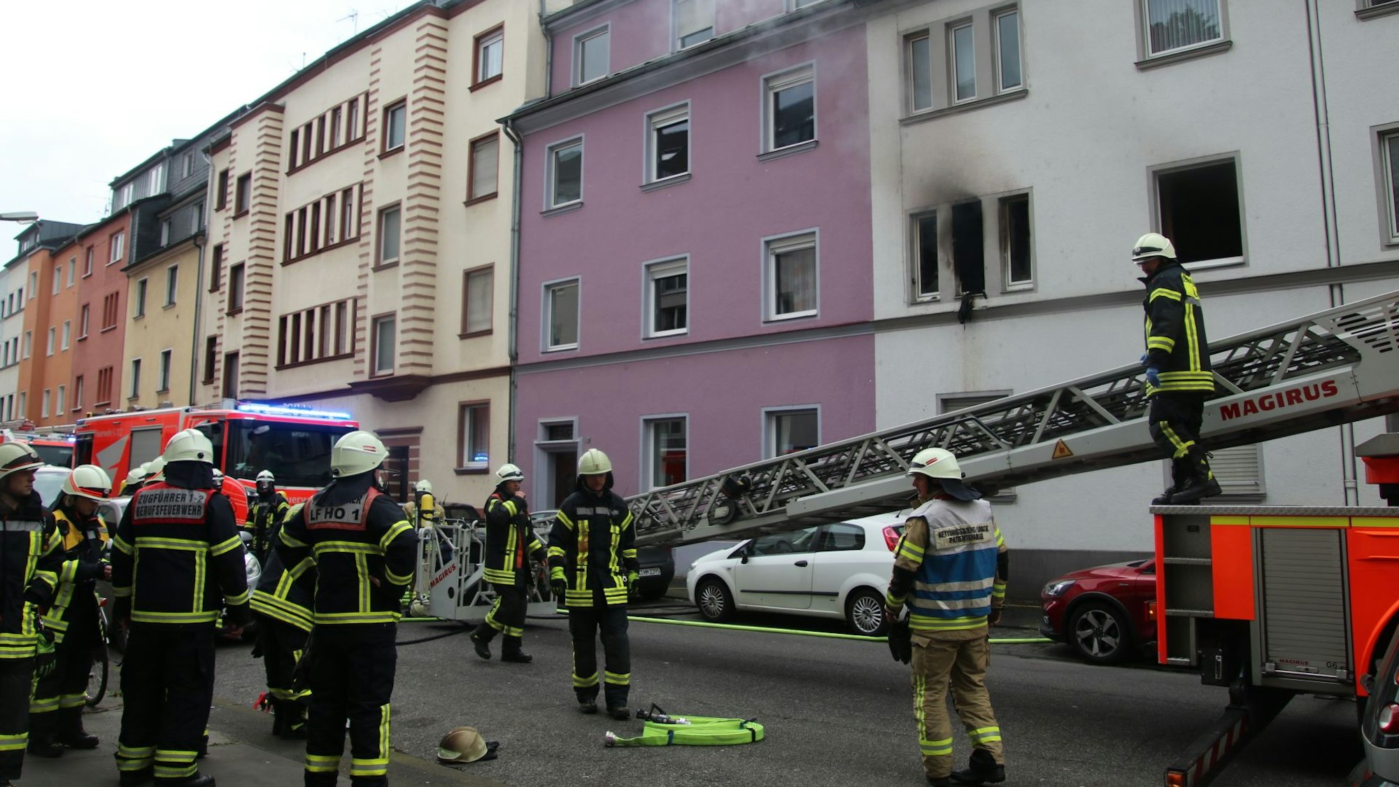 Feuerwehrleute stehen vor einem Haus, aus dessen Fenstern Rauch aufsteigt.