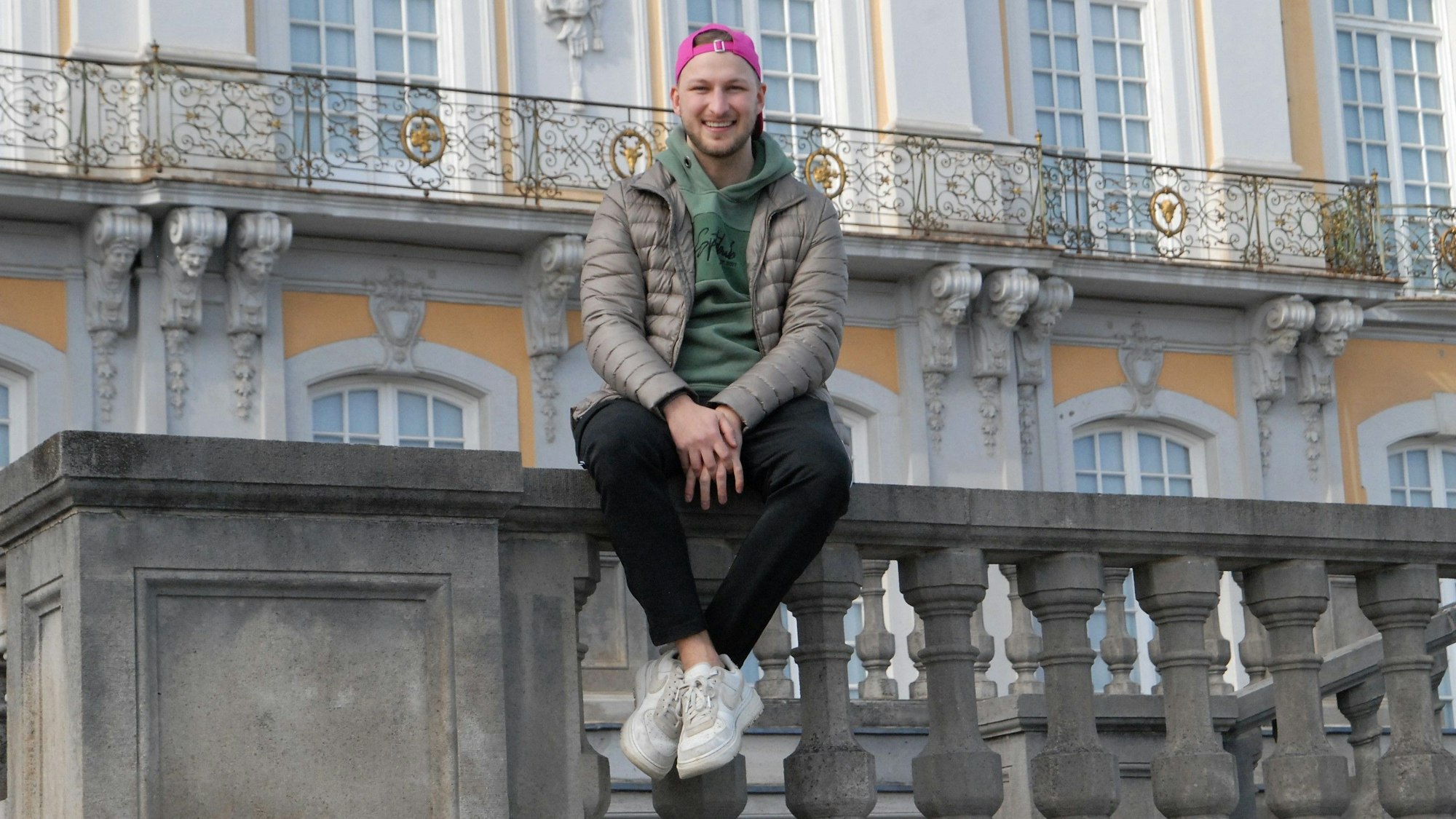 Auf dem Fot ist DSDS-Teilnehmer David Leischik vor dem Schloss in Brühl zu sehen. Er sitzt auf einem Geländer.
