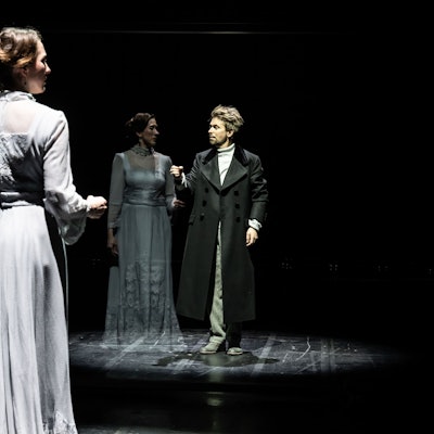 Emily Hindrichs trägt ein helles Kleid, Miljenko Turk einen schwarzen Mantel. Sie stehen auf der verdunkelten Bühne des Staatenhauses.