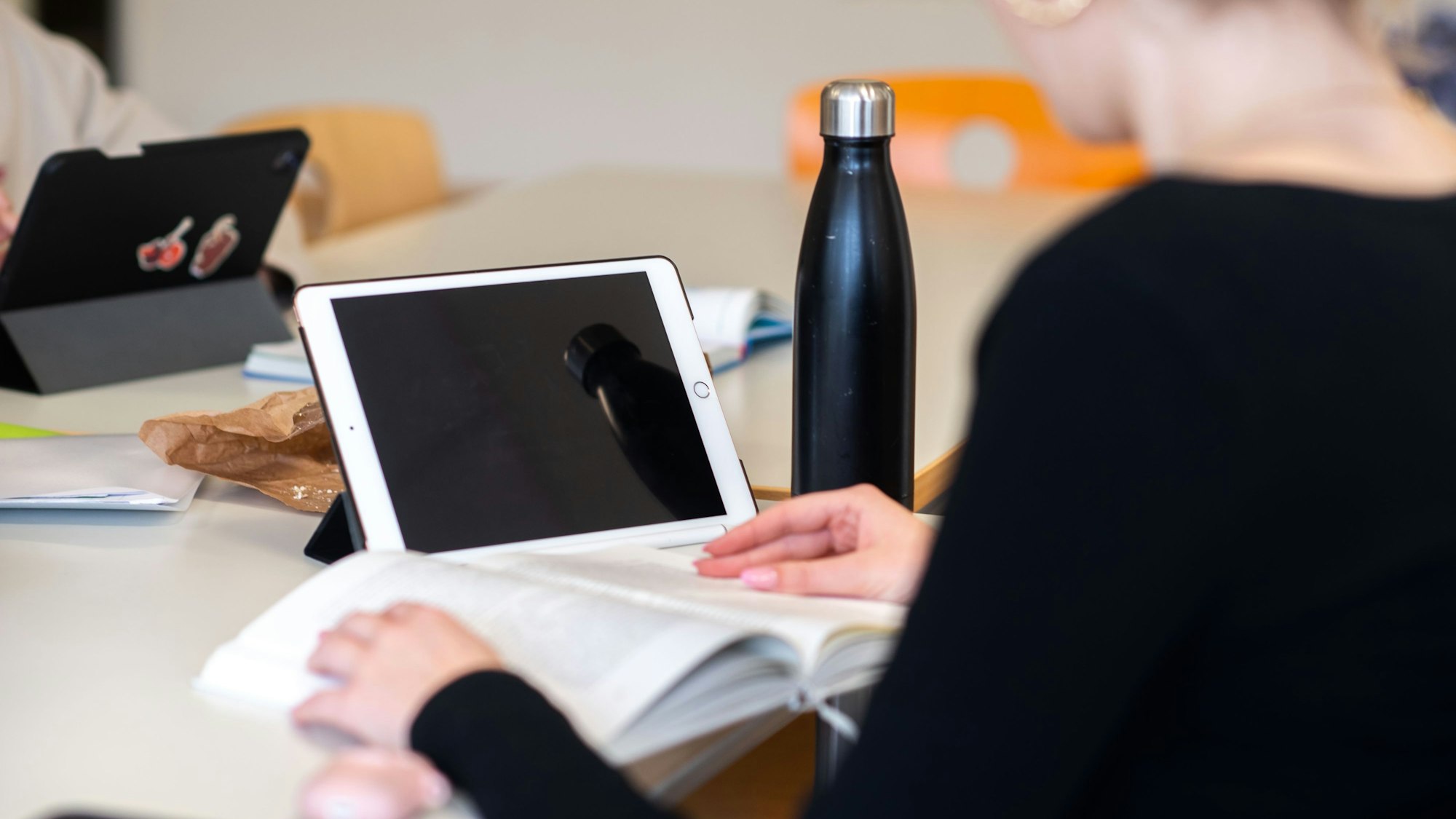 Eine Schülerin hat ein Buch und ein iPad vor sich auf dem Tisch liegen.