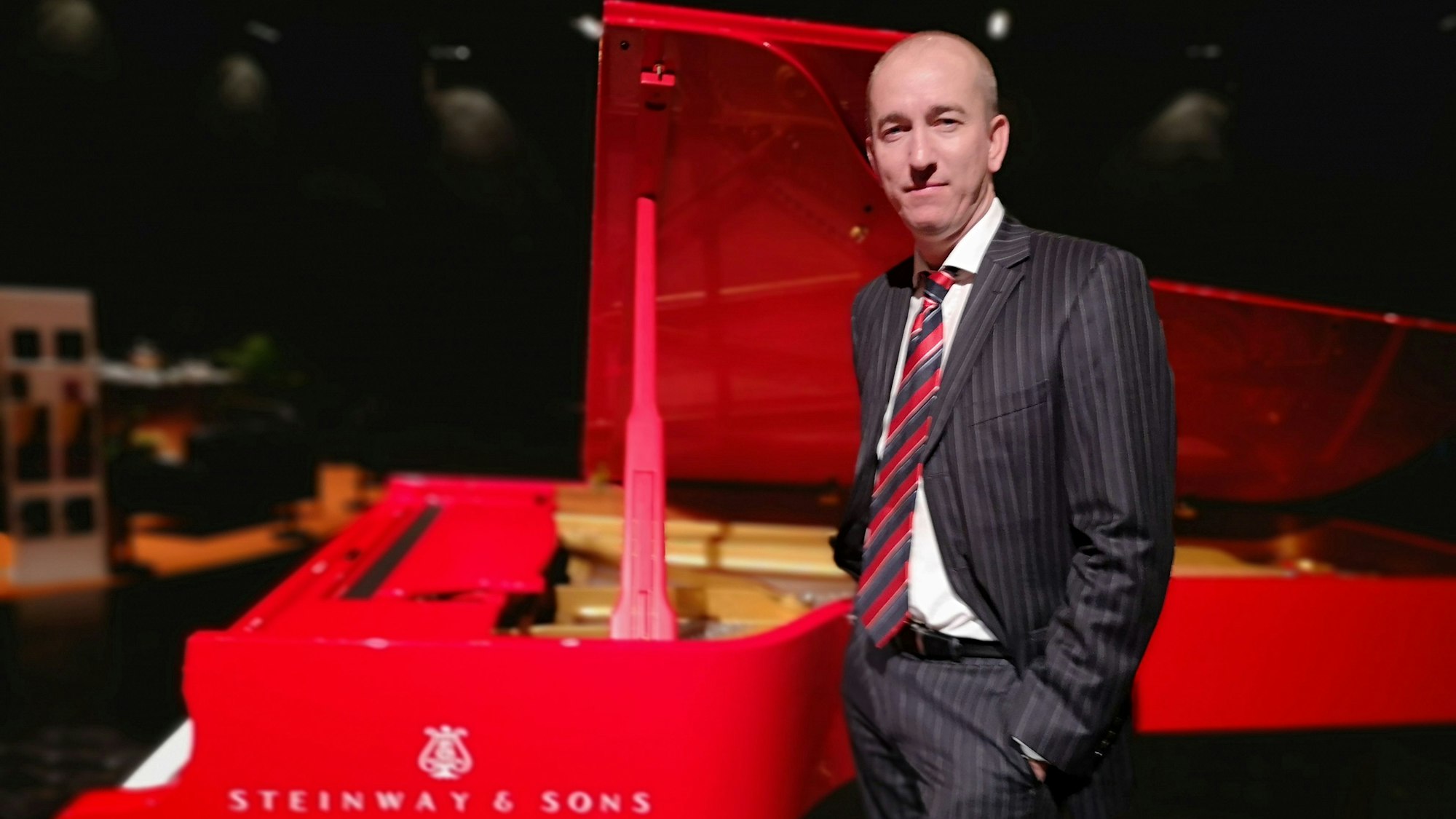 Der amerikanische Pianist Chris Hopkins spielt am 1. Mai in der Ülepooz. Er steht im Anzug vor einem roten Flügel.