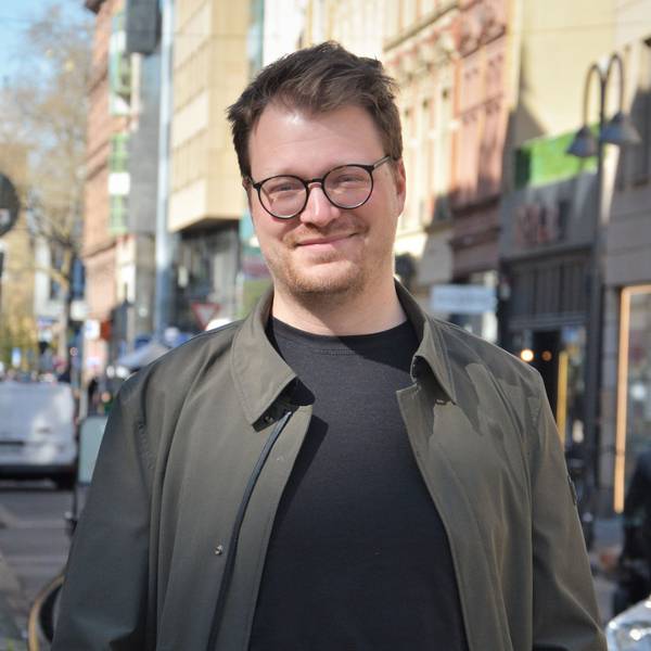 Maxi Gstettenbauer steht in der Sonne auf der Ehrenstraße in Köln und lächelt in die Kamera.