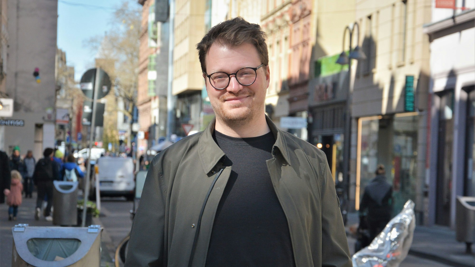 Maxi Gstettenbauer steht in der Sonne auf der Ehrenstraße in Köln und lächelt in die Kamera.