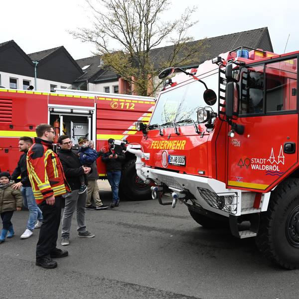 Es ist ein Fahrzeug der Waldbröler Feuerwehr zu sehen. Neben diesem stehen mehrere Menschen.