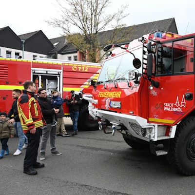 Es ist ein Fahrzeug der Waldbröler Feuerwehr zu sehen. Neben diesem stehen mehrere Menschen.