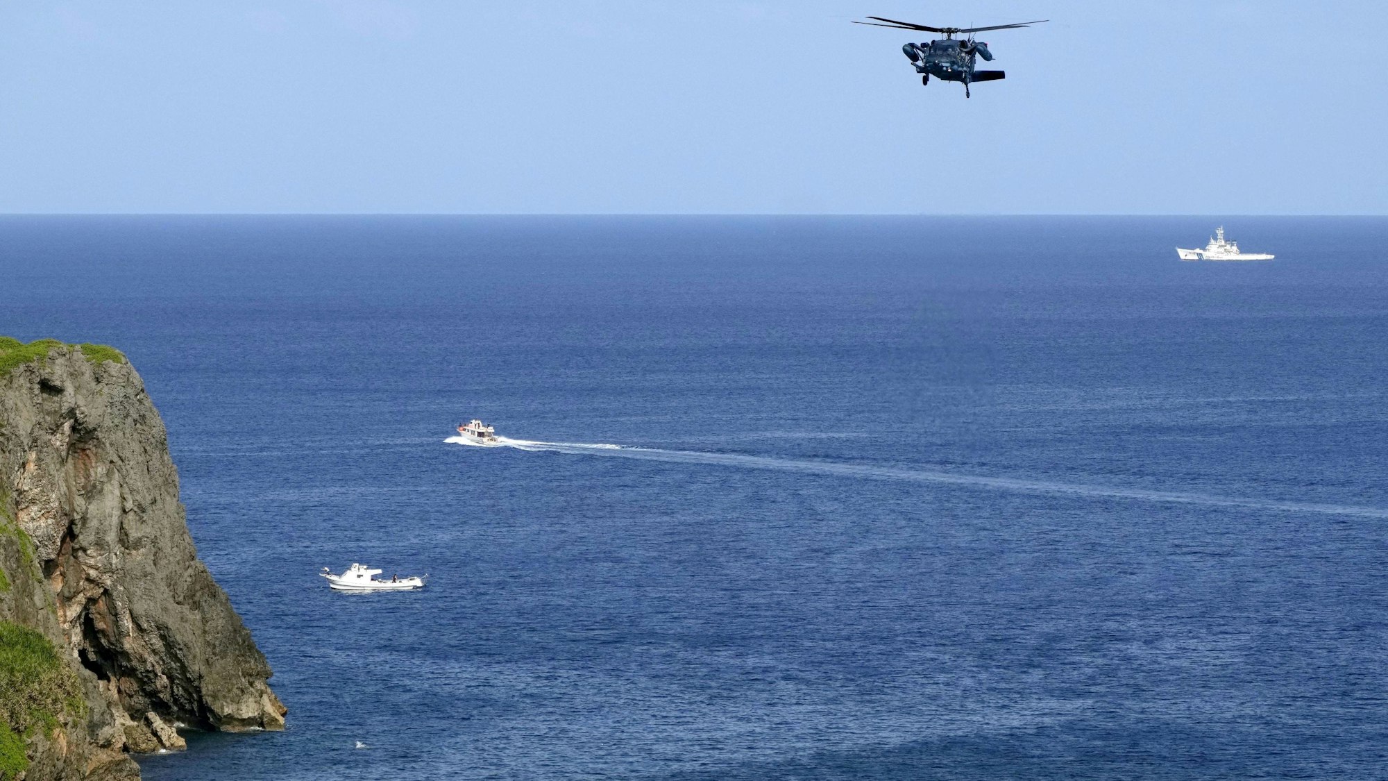 Ein Hubschrauber sucht die Gewässer vor einer Insel ab.