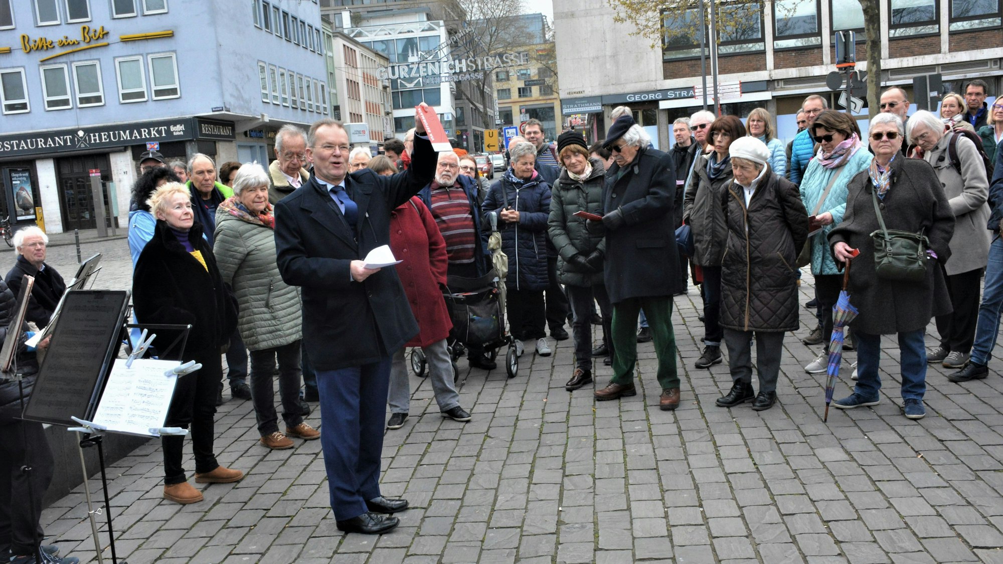 Stadtsuperintendent Bernhard Seiger steht auf dem Heumarkt und zeigt den Teilnehmern an einer Führung den Flyer zur Via Reformata.