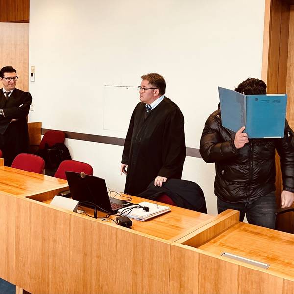 Ein Angeklagter steht neben seinen Anwälten im Gerichtssaal.