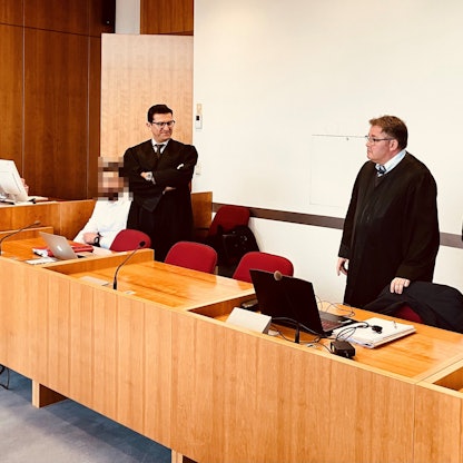 Ein Angeklagter steht neben seinen Anwälten im Gerichtssaal.