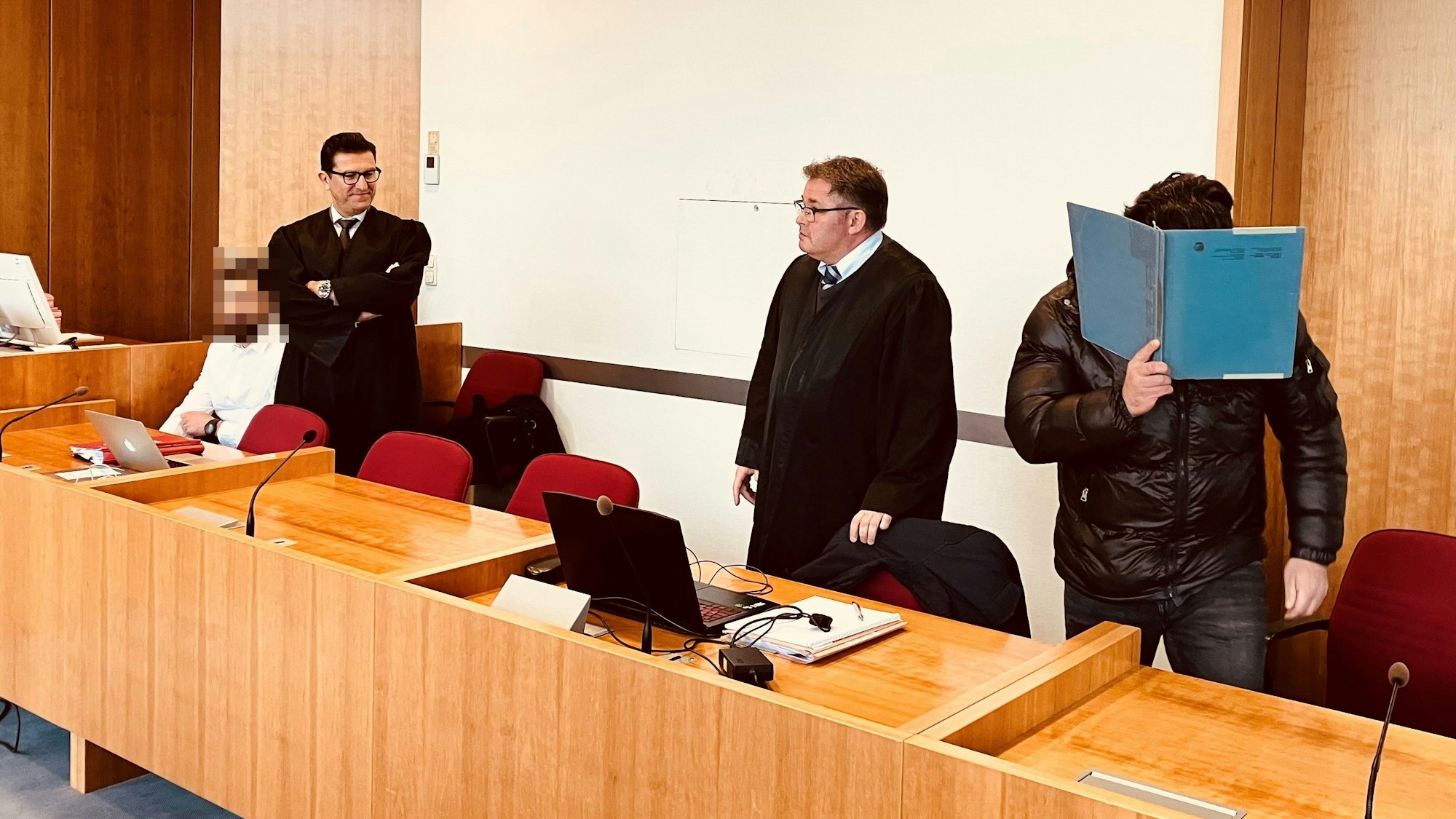 Angeklagte und Verteidiger sitzen und stehen im Gericht.