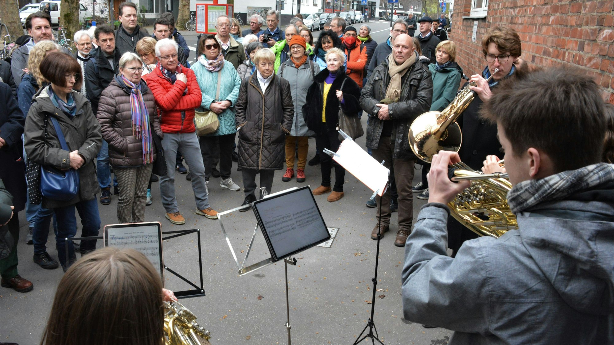 Vor einer Gruppe Menschen stehen vier junge Leute, die Blasinstrumente spielen.