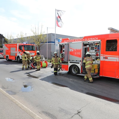 Feuerwehrfahrzeuge stehen auf einer gesperrten Straße. Feuerwehrleute laden Einsatzgerät aus.