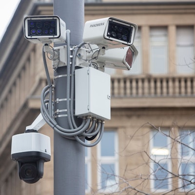 Mehrere Kameras an einer Laterne, dahinter ein älteres Gebäude.