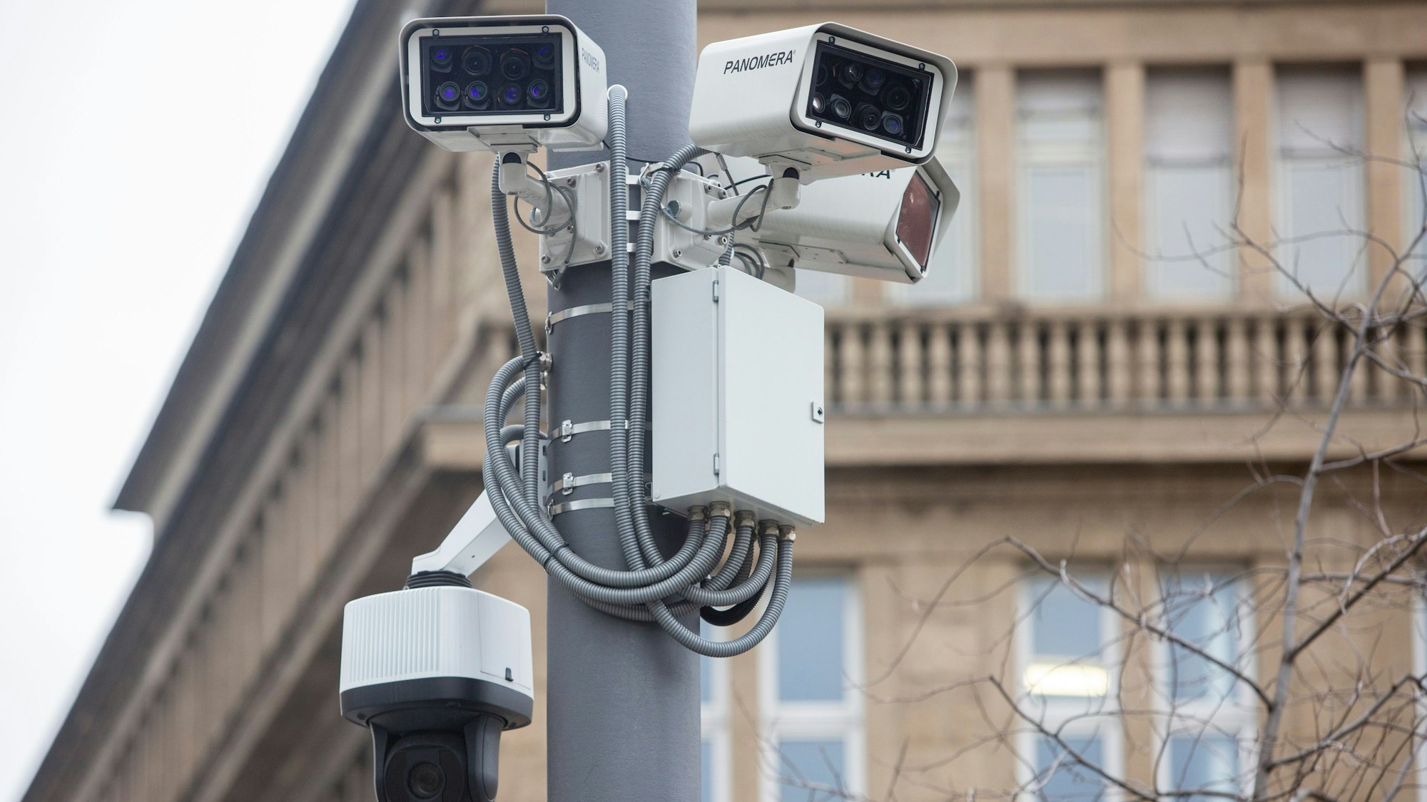 Mehrere Kameras an einer Laterne, dahinter ein älteres Gebäude.