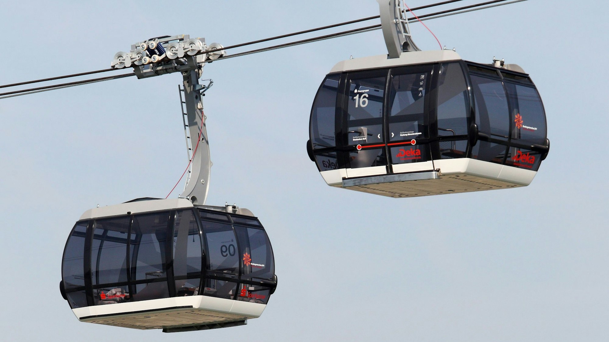 Zwei große Seilbahngondeln schweben vor blauem Himmel.