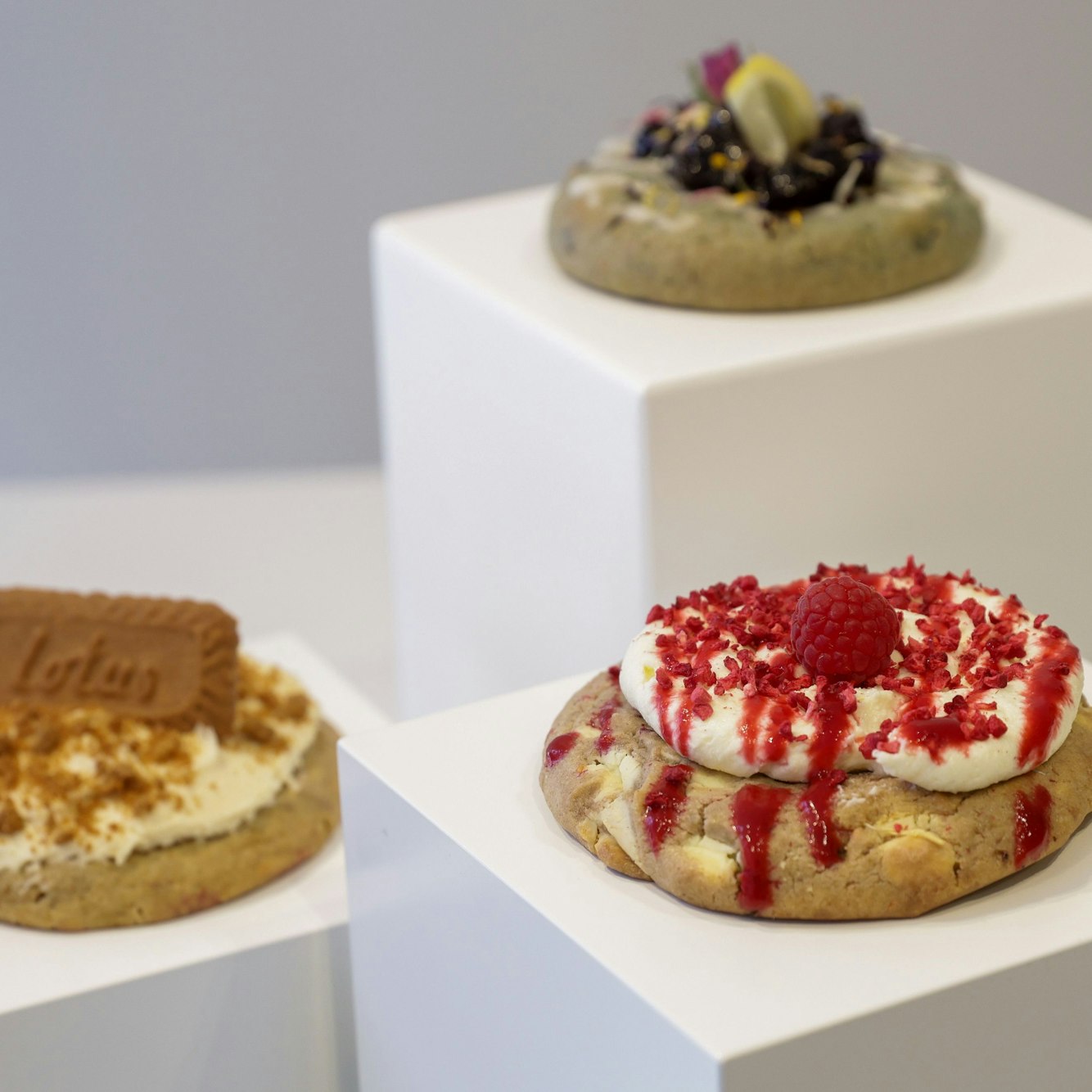 Drei verzierte Cookies liegen auf weißen Podesten.