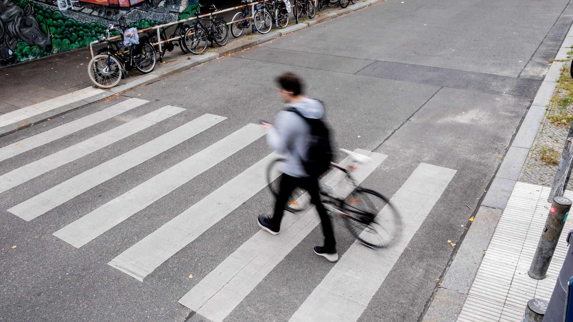 Ein Fahrradfahrer schiebt sein Fahrrad über einen Zebrastreifen.