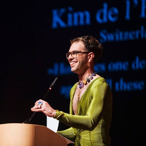 Kim de l'Horizon steht am Mikrofon mit einem grünen Kleid und Schmuck.