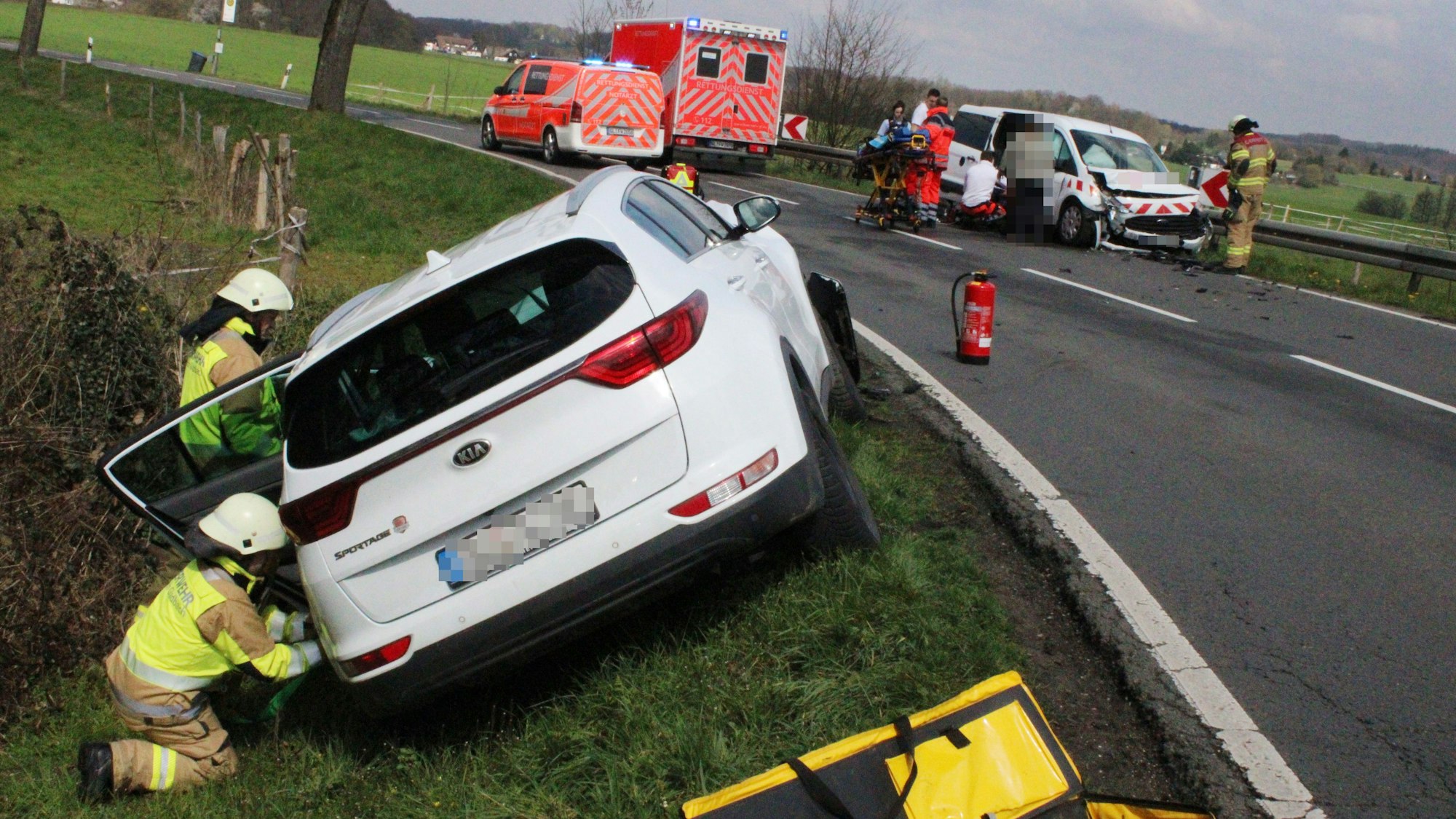 Schwer beschädigte Autos stehen neben einer Straße. Feuerwehrleute und Rettungsdienstmitarbeitende sind im Einsatz.