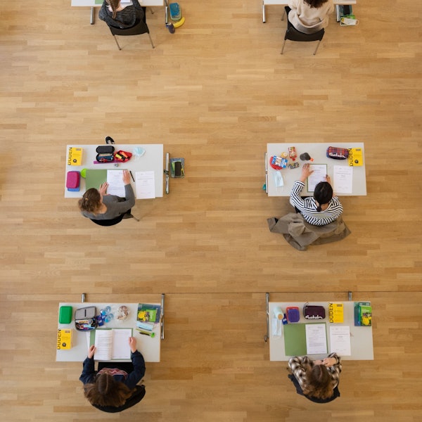 Schüler sind während der Abiturprüfung aus der Vogelperspektive zu sehen. Sie sitzen an weißen Tischen, auf denen je ein Duden liegt, Schreibzeug und die Aufgabenmappe.