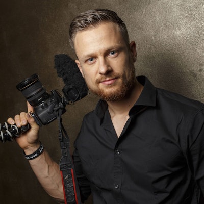 Youtuber und Survival-Experte Fritz Meinecke blickt in die Kamera. Er hält bei einem Fotoshooting eine Kamera mit Stativ in der Hand.