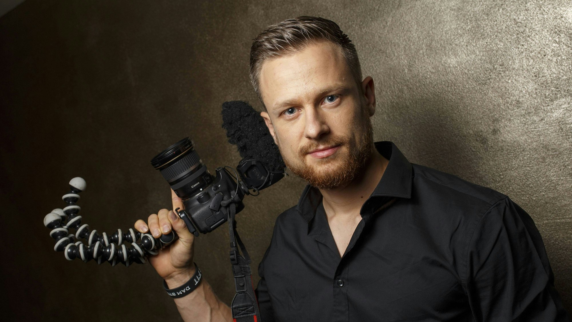 Youtuber und Survival-Experte Fritz Meinecke blickt in die Kamera. Er hält bei einem Fotoshooting eine Kamera mit Stativ in der Hand.