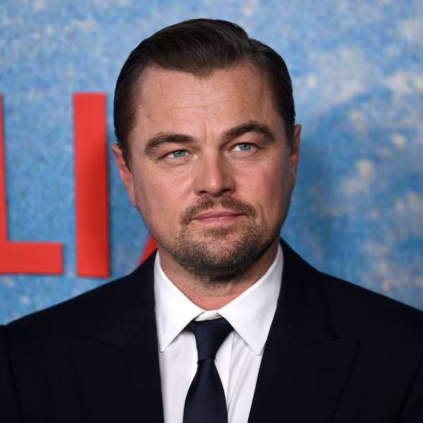 Schauspieler Leonardo Di Caprio blickt auf dem Roten Teppich in die Kamera. Er trägt einen schwarzen Anzug.