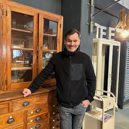 Mann vor einer antik aussehenden Kommode mit Glasvitrine