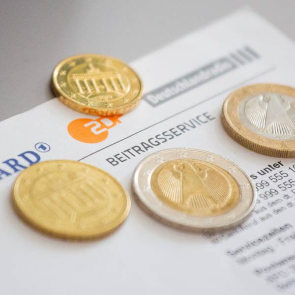 Euromünzen liegen auf einem Anschreiben zur Anmeldung für die Rundfunkgebühren, neben den Logo von ARD, ZDF und Deutschlandfunk.