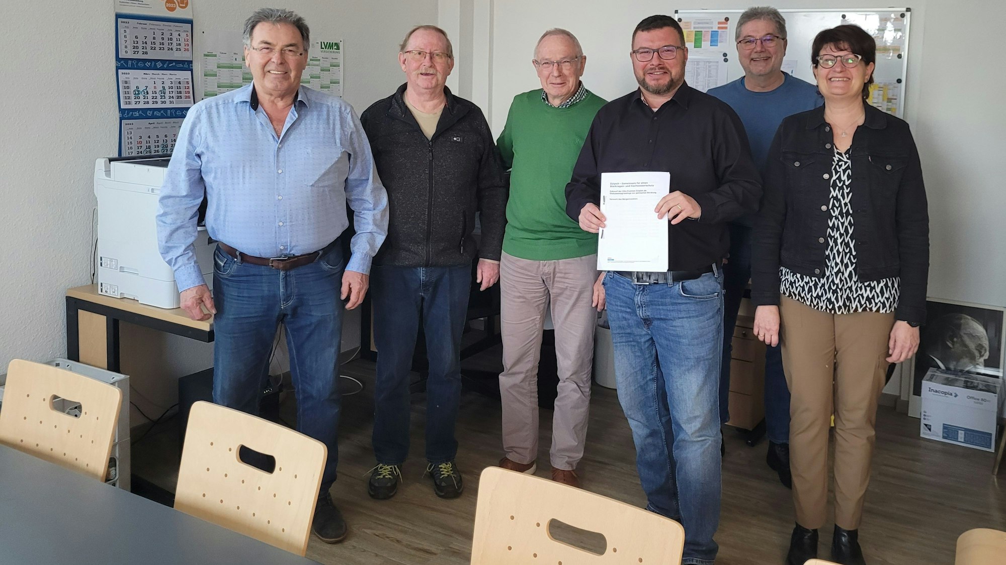 Mehrere Personen stehen zusammen, eine hält ein Papier in der Hand.