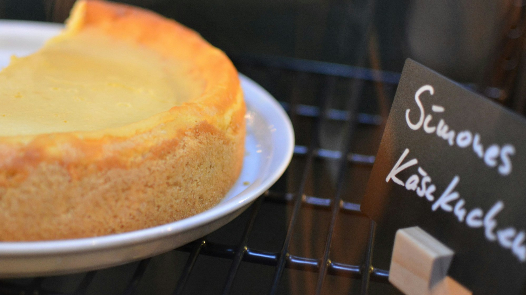 Ein Käsekuchen auf einem Teller, daneben ein Schild auf dem Simones Käsekuchen steht.