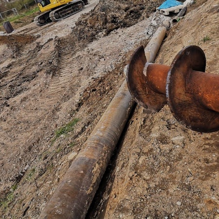 Ein großer Bohrer, umgeben von Erde, auf einer Baustelle.