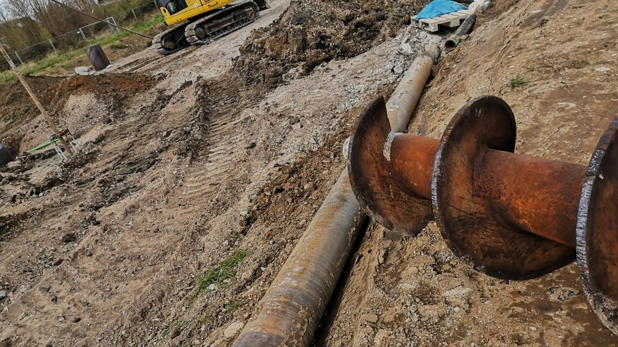 Ein großer Bohrer, umgeben von Erde, auf einer Baustelle.