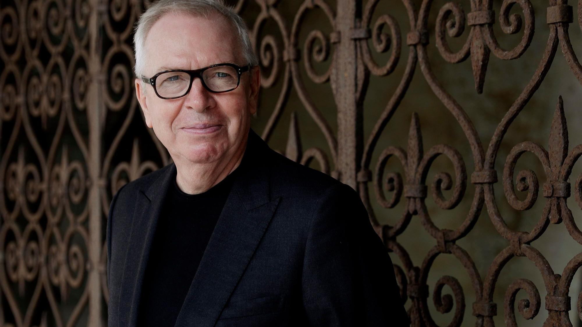 Der britische Architekt David Chipperfield schaut in die Kamera. Er trägt eine Brille und einen schwarzen Anzug.