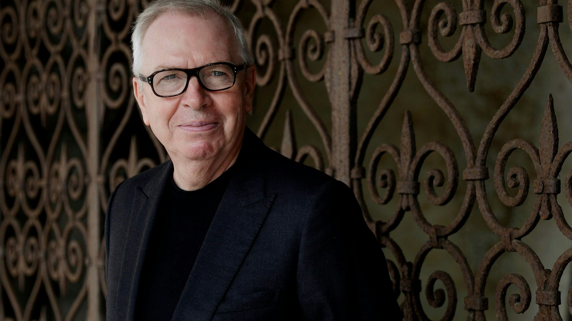Der britische Architekt David Chipperfield schaut in die Kamera. Er trägt eine Brille und einen schwarzen Anzug.